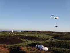 P2011DSC07954	A helicopter dropping off bags of chopped heather, with The Edge trig pillar below.